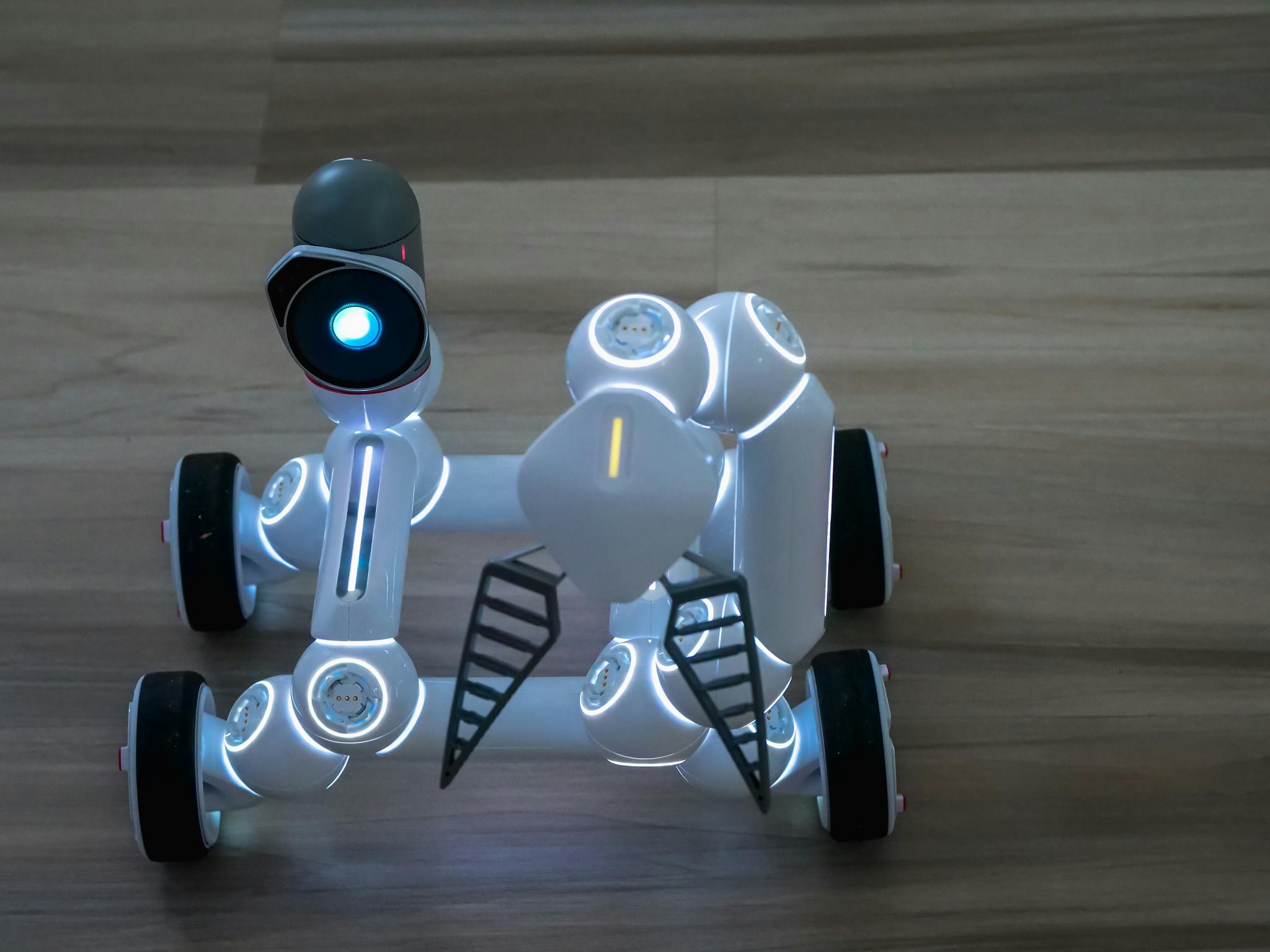 Close-up of a wheeled robot toy on a wooden surface indoors.